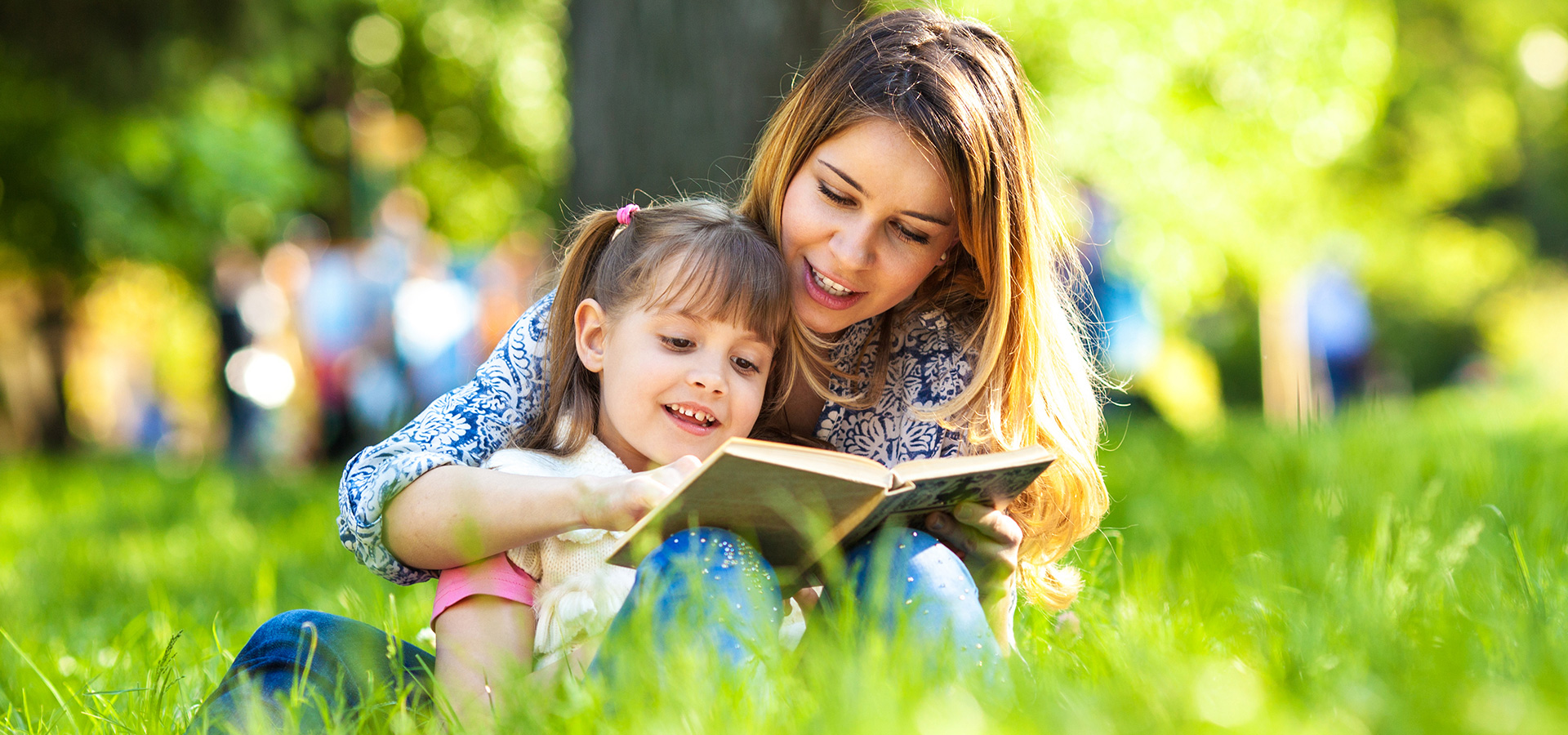 Mother reading to her daughter under the trees